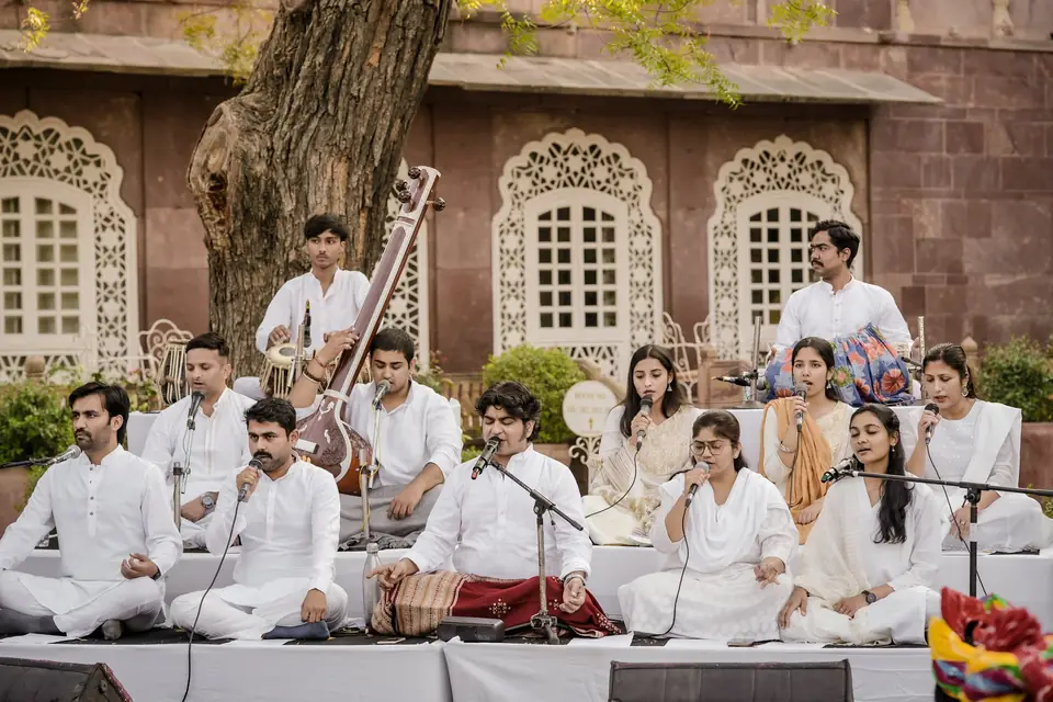 A vocal ensemble in white performing in front of the haveli&rsquo;s carved windows