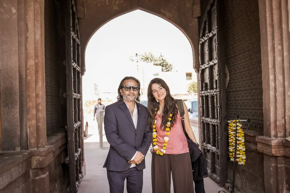 Two guests in marigold garlands under the carved gateway