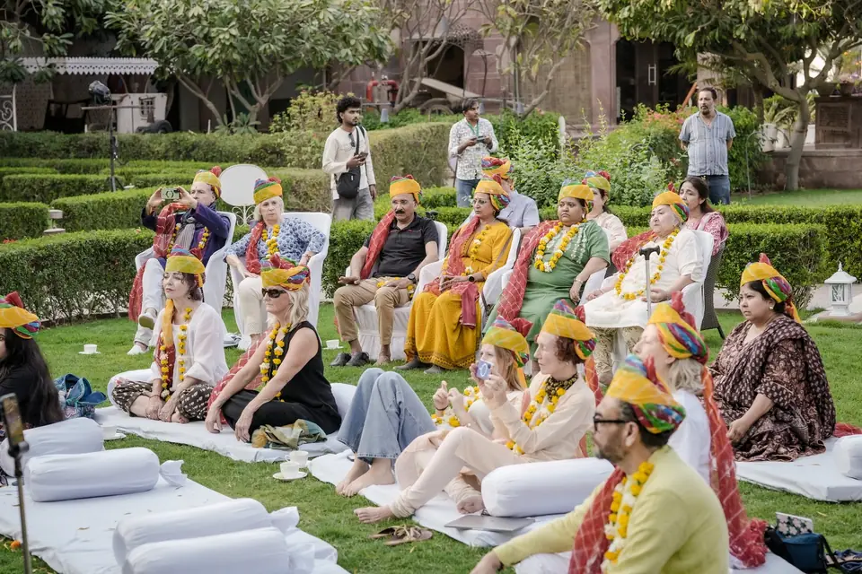 Guests in turbans and garlands seated on white bolsters on the lawn