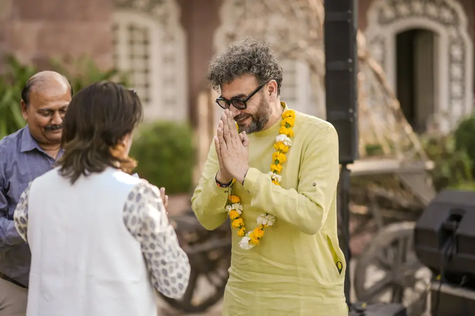 A guest in a marigold garland greeting another with folded hands