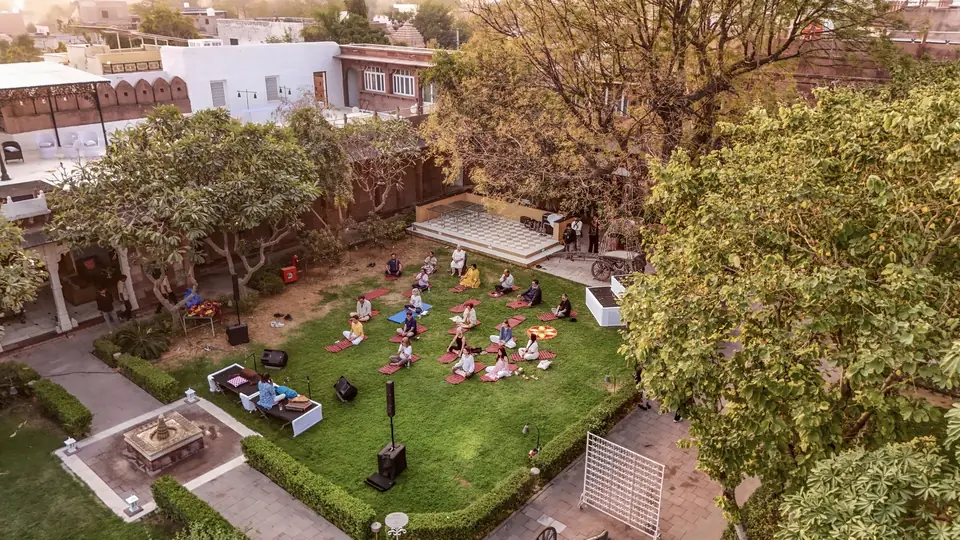 The lawn and its trees from above, guests on red mats in the early light