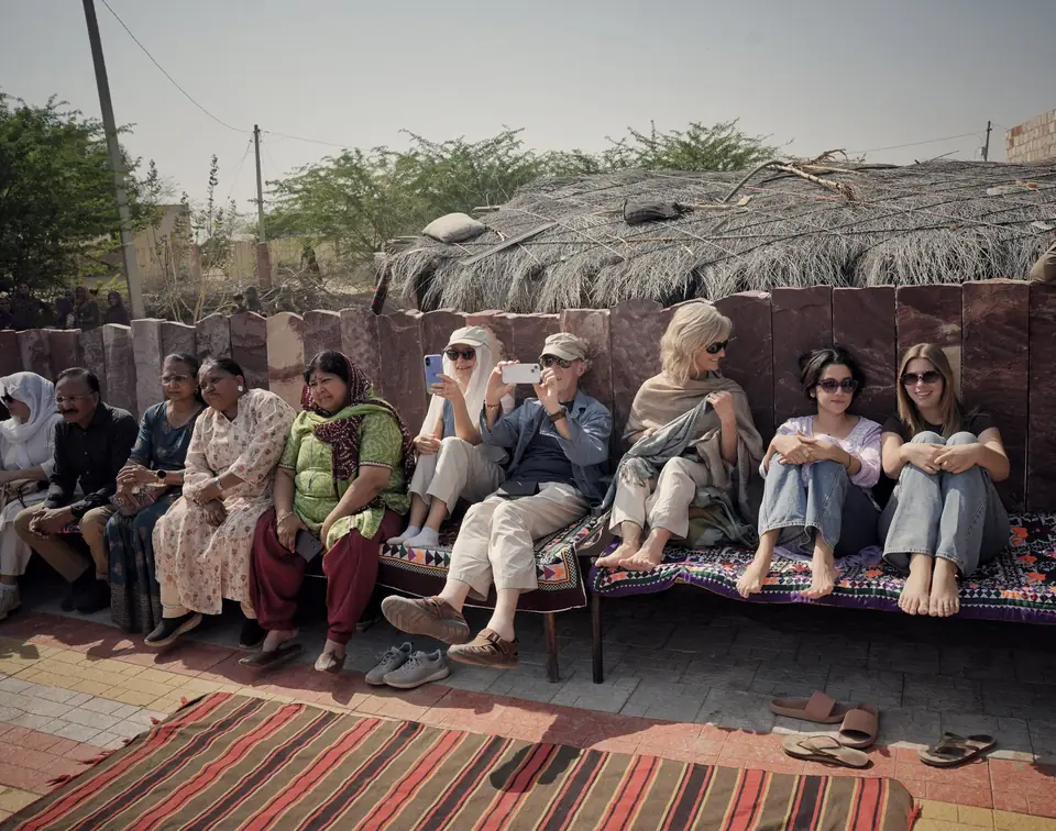 Guests seated on carpets along a wall, listening