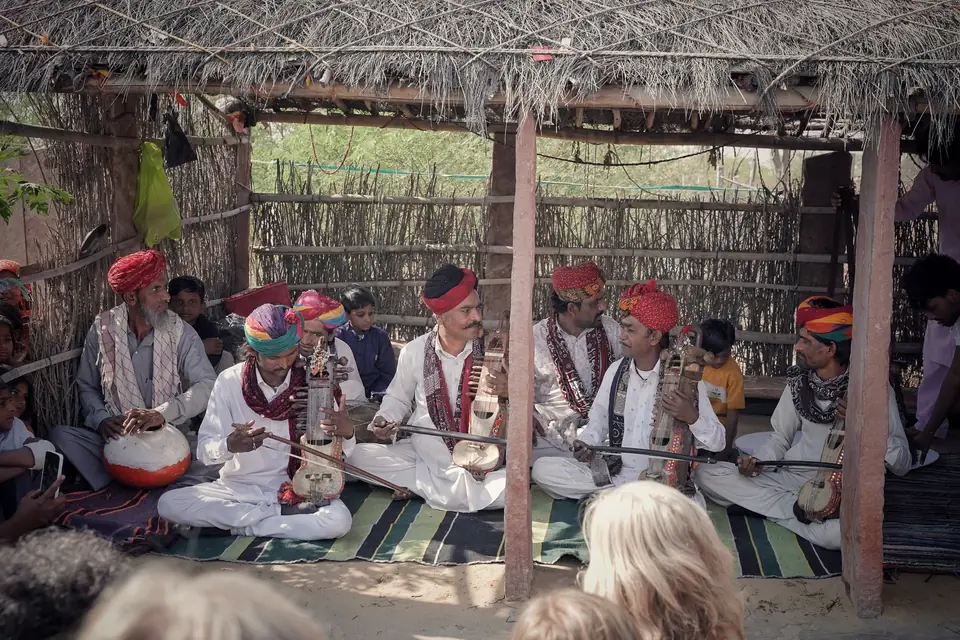 Folk musicians in turbans playing under a thatched shelter