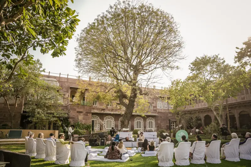 A daytime concert in the garden at Pal Garh, guests in white chairs beneath a great tree and the haveli behind